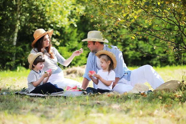 Glückliche Familie mit Kindern beim Picknick im Park Eltern mit Kindern sitzen auf Gartengras und essen Wassermelone im Freien