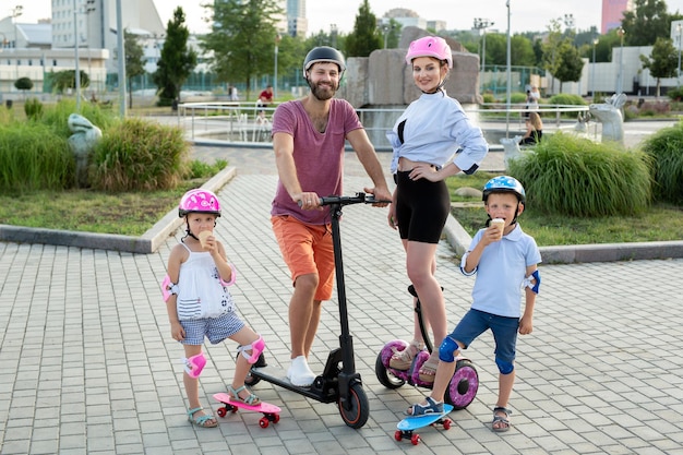 Glückliche Familie mit Kindern, die auf Segways-Elektrorollern und Skateboards im Park fahren