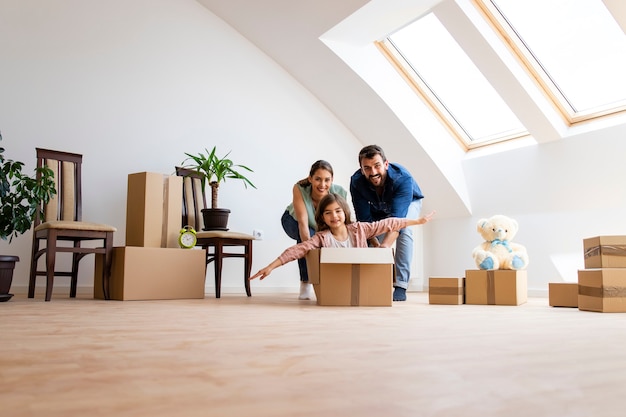 Glückliche Familie mit Kindern, die den ersten Tag im neuen Haus genießen und in Kartons reiten