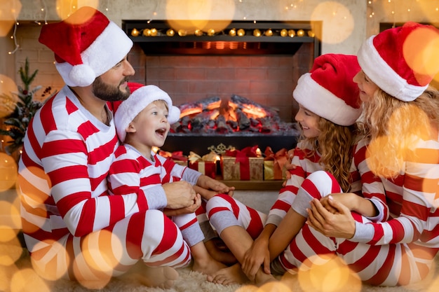 Glückliche Familie mit Kindern, die gestreiften Pyjama nahe Kamin an Weihnachten tragen. Mutter, Vater und Kinder haben Spaß zu Hause.