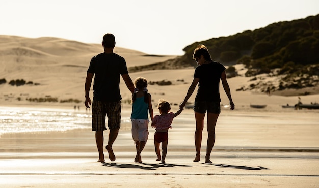 Glückliche Familie mit Kindern Silhouette bei Sonnenuntergang am Meeresstrand Vater Mutter und Kinder spazieren am Meeresufer mit Abendsonnenlicht