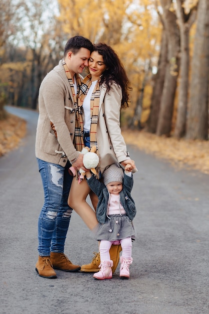 Glückliche Familie mit kleinem Baby gehen an der Parkstraße mit gelben Bäumen am Herbst