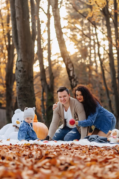 Glückliche Familie mit kleinem nettem Kind im Park auf gelbem Blatt mit großem Kürbis im Herbst