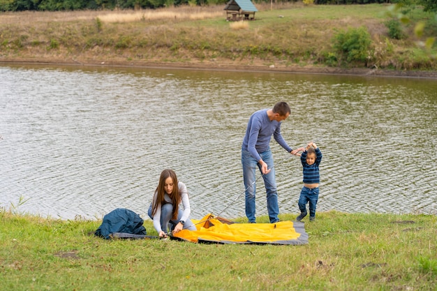 Glückliche Familie mit kleinem Sohn Camping Zelt aufbauen, Glückliche Kindheit, Campingausflug mit den Eltern, Ein Kind hilft beim Aufbau eines Zeltes