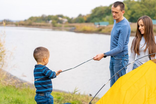 Glückliche Familie mit kleinem Sohn errichtete Campingzelt. Glückliche Kindheit, Campingausflug mit den Eltern. Ein Kind hilft beim Aufbau eines Zeltes