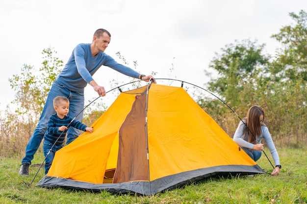 Glückliche Familie mit kleinem Sohn stellte Campingzelt auf. Glückliche Kindheit, Campingausflug mit den Eltern. Ein Kind hilft beim Aufbau eines Zeltes