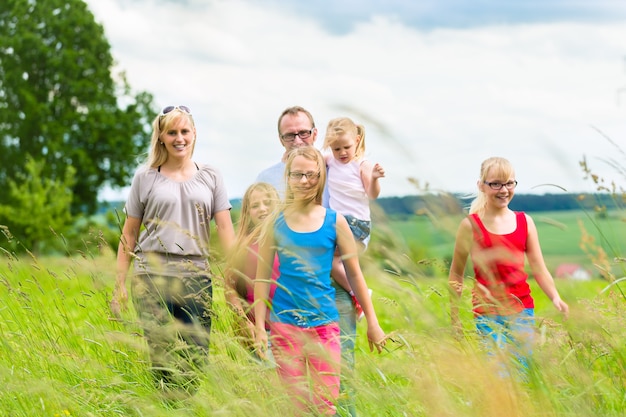 Glückliche Familie mit Mädchen oder Töchtern, die im Sommer auf einer Wiese gehen