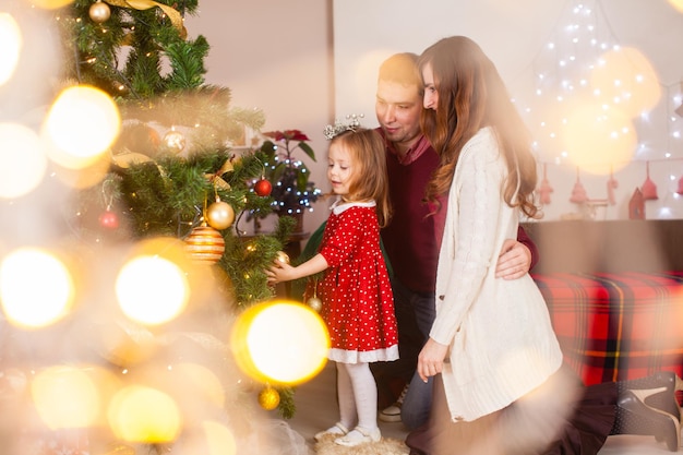 Glückliche Familie mit Tochter schmücken den Weihnachtsbaum. Feiertagsabend