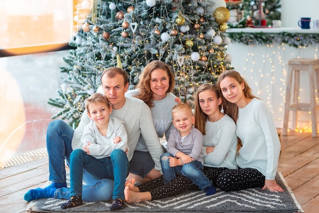 Glückliche Familie mit vier Geschwistern in der Nähe des Weihnachtsbaums mit den Geschenkboxen. Weihnachtsfamilienmorgen, Weihnachtsstimmungskonzept