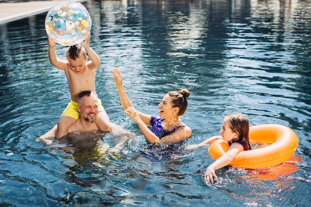Glückliche Familie mit zwei Kindern, die sich im Schwimmbad amüsieren Sommerurlaubskonzept