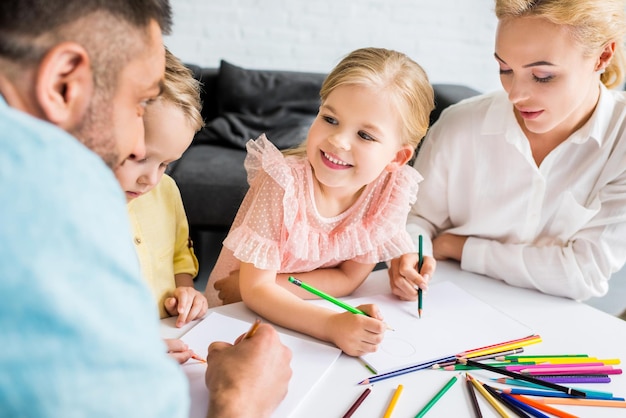 glückliche Familie mit zwei Kindern, die zu Hause mit Buntstiften zeichnen