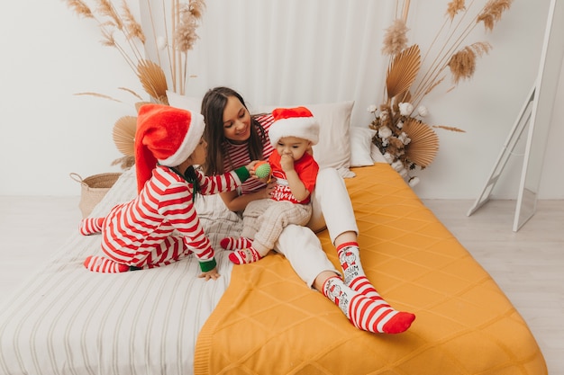 Glückliche Familie, Mutter und Kinder in Pyjamas und Weihnachtsmützen, die Spaß auf dem Bett haben. Weihnachten