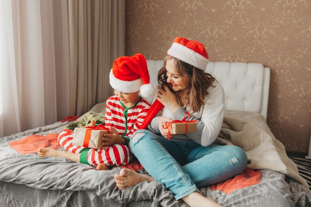 Glückliche Familie, Mutter und Sohn, die am Weihnachtsmorgen im Bett umarmt und Geschenke gibt. Weihnachten.