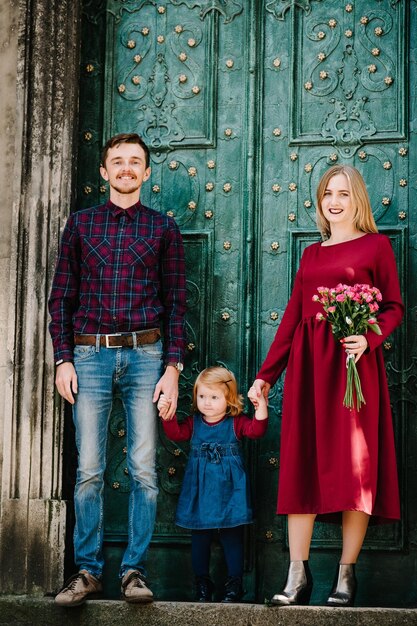 Glückliche Familie, Mutter, Vater, Tochter mit Blumenstrauß, die Zeit zusammen genießt, steht auf dem Hintergrund der alten Tür des alten Gebäudes auf der Straßenstadt im Land Europa