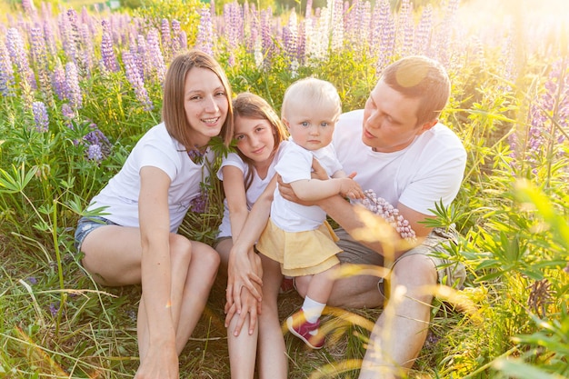 Glückliche Familie Mutter Vater umarmt Kinder im Freien Frau Mann Baby Kind und Teenager-Mädchen sitzt auf Sommerfeld mit blühenden Blumen Hintergrund Glückliche Familie, Mutter, Vater und Töchter, die auf der Wiese spielen