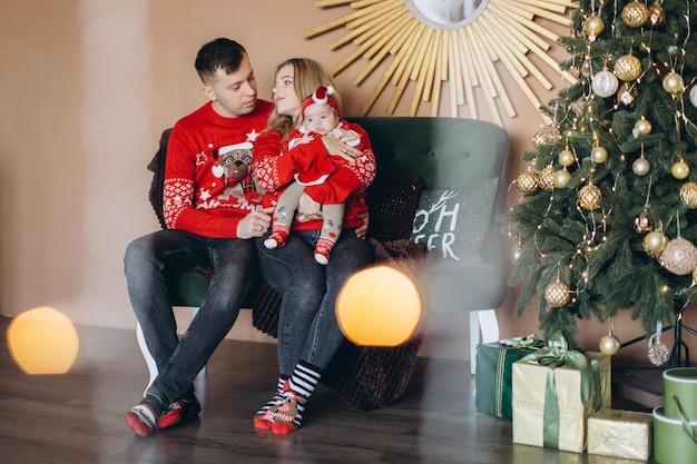 Glückliche Familie, Mutter, Vater und kleine Tochter in roter traditioneller Weihnachtskleidung verbringen Zeit zusammen in der Nähe des Weihnachtsbaum-Kopienraums