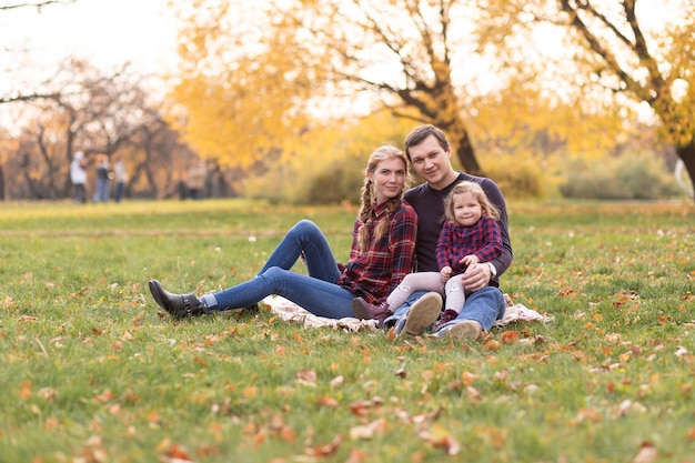 Foto glückliche familie ruht sich im herbstwald aus. mama, papa und tochter sitzen im herbstpark.