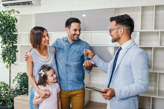 Glückliche Familie spricht mit einem Immobilienmakler über einen Schlüssel ihres neuen Zuhauses.