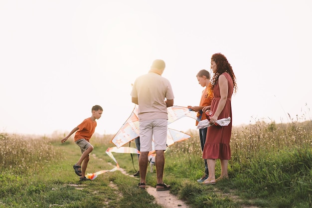 Glückliche Familie und Kinder laufen auf der Wiese mit einem Drachen im Sommer in der Natur Familie spielt mit Drachen, während sie entlang des ländlichen Sommerfeldes läuft Familientag