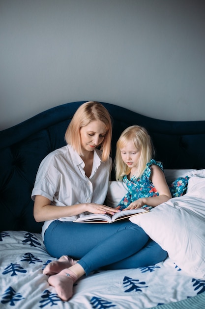 Glückliche Familie von blonder Mutter und Tochter liest ein Buch im Bett.