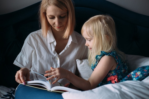 Glückliche Familie von blonder Mutter und Tochter liest ein Buch im Bett.