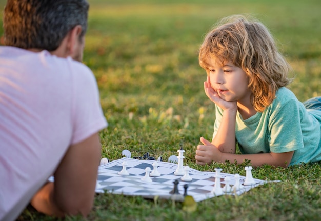 Glückliche Familie von Eltern und Sohn, die Schach auf grünem Gras in der kindlichen Entwicklung des Parks im Freien spielen