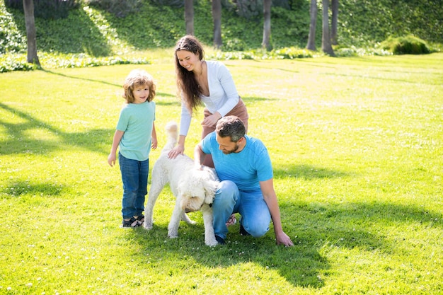 Glückliche Familie von Mutter, Papa und Kind, die mit Hund im grünen Gras des Sommerparks spielen, entspannen Sie sich