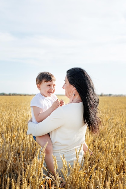 Glückliche Familie von Mutter und Kleinkind, die auf dem Familienporträt des Weizenfeldes spazieren gehen