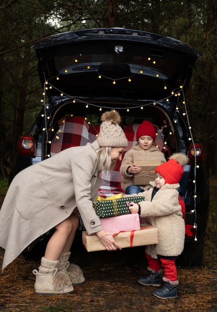 Glückliche Familie von Mutter und zwei Kindern mit Weihnachtsgeschenkboxen, die im weihnachtlich dekorierten Auto sitzen