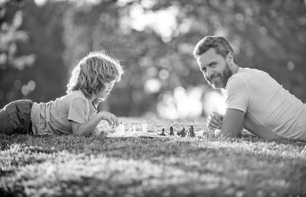 Glückliche Familie von Vater, Mann und Sohn, die Schach auf grünem Gras im logischen Sport des Parks im Freien spielen