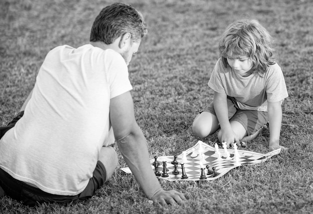 Glückliche Familie von Vater, Mann und Sohn, die Schach auf grünem Gras im Park im Freien spielen