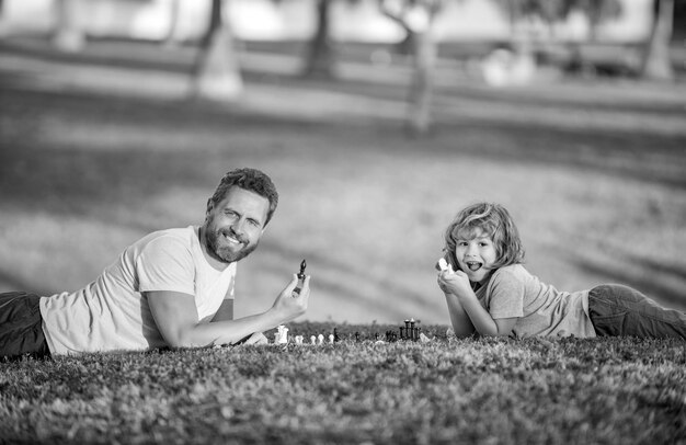 Glückliche Familie von Vater, Mann und Sohn spielen Schach auf grünem Gras im Park im Freien Vaterschaft