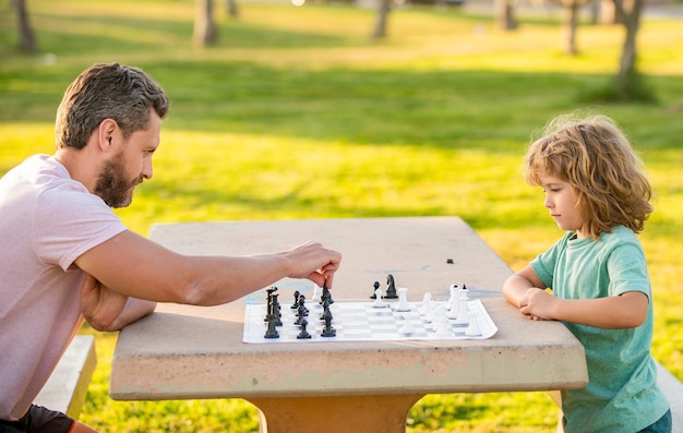 Glückliche Familie von Vater und Sohn spielen Schach auf dem Tisch im Park im Freien, Logik.