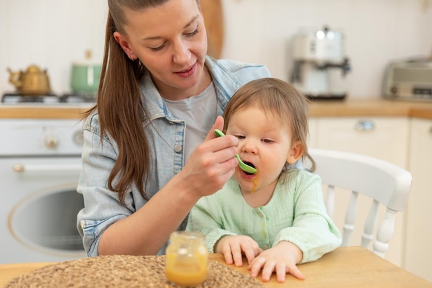 Glückliche Familie zu Hause Mutter füttert ihr Baby mit dem Löffel in der Küche kleines Kleinkind mit