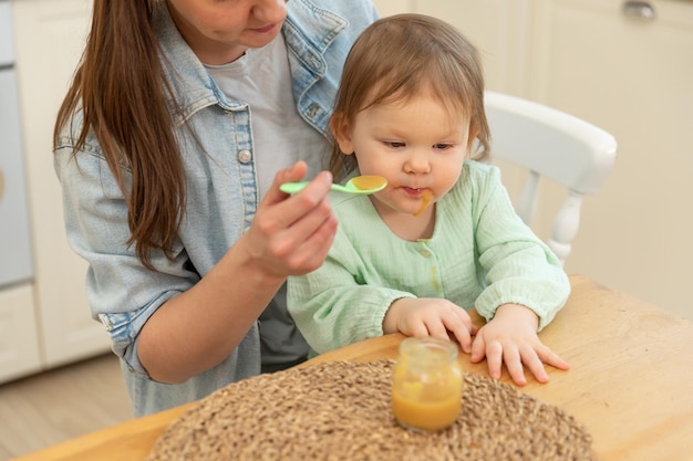 Glückliche Familie zu Hause Mutter füttert ihr Baby vom Löffel in der Küche kleines Kleinkind Kind mit