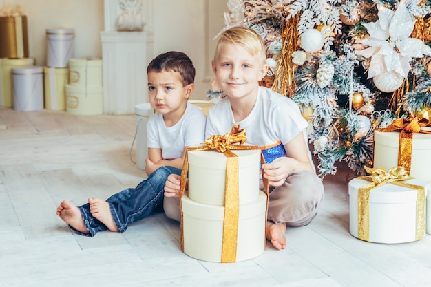 Glückliche Familie zwei Kinder Junge entspannen sich am Heiligabend zu Hause in der Nähe des Weihnachtsbaumes zu spielen. Brüder im hellen Raum mit Winterdekoration Weihnachten Neujahr Zeit zum Feiern.