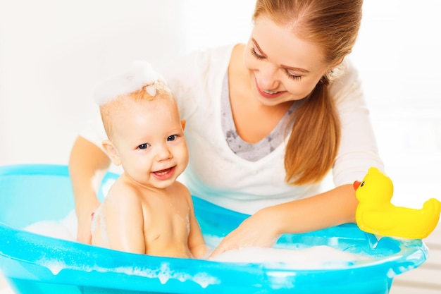 Glückliche Familienmutter badet das Baby in einem blauen Bad