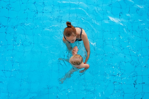 Glückliche Familienmutter bringt ihrer Tochter bei, in der Draufsicht des Pools zu schwimmen