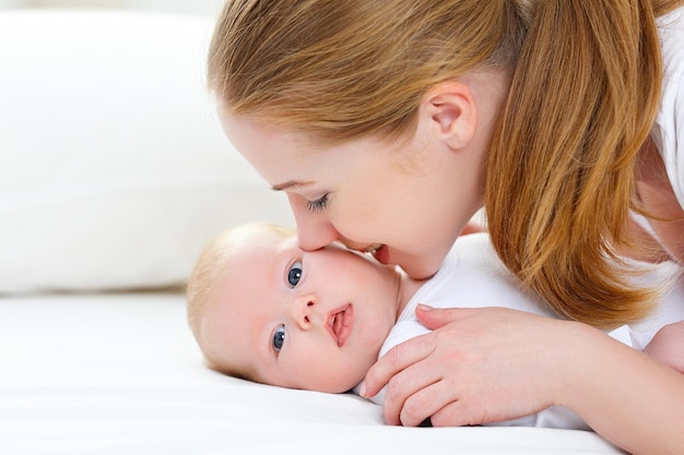 Glückliche Familienmutter, die ihr neugeborenes Baby im Bett küsst