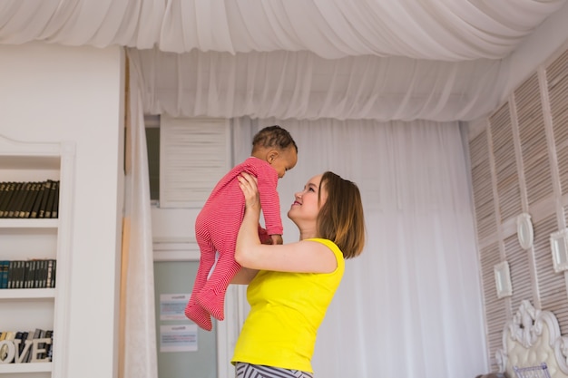 Glückliche Familienmutter erbricht gemischtes Baby, das zu Hause spielt playing