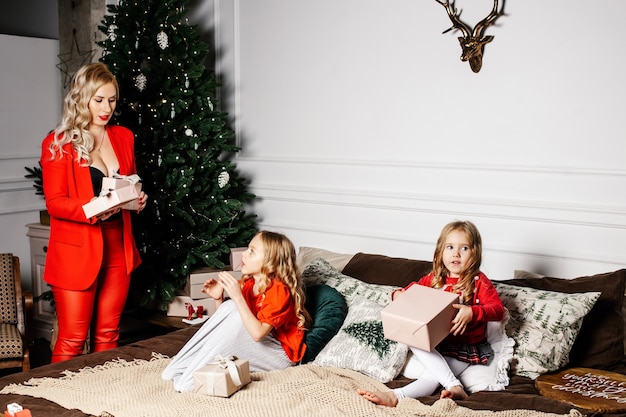 Glückliche Familienmutter geben Geschenkboxen zu ihren Töchtern in einem Raum mit Weihnachtsdekoration zu Hause.