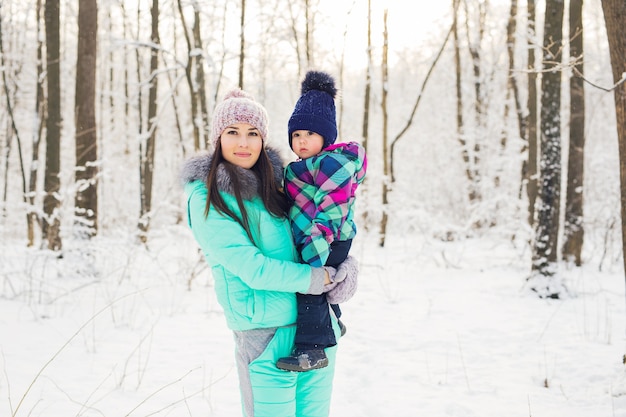 Glückliche Familienmutter und Babytochter, die im Winter draußen im Schnee spielt und lacht.