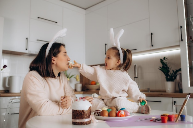 Glückliche Familienmutter und Kindermädchen malen Eier für Ostern zu Hause