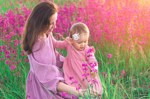 Glückliche Familienmutter und kleine Tochter 2 Jahre alt, die auf einem Feld mit wilden Wildblumen spielen