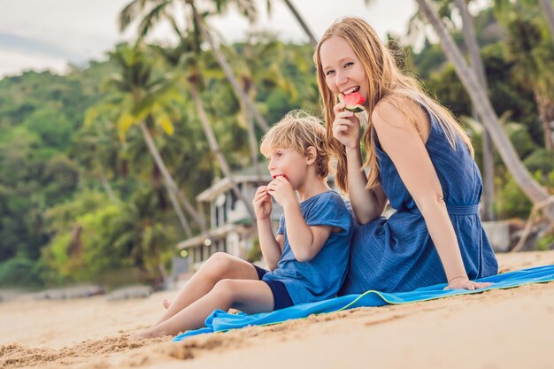 Glückliche Familienmutter und Sohn, die eine Wassermelone am Strand essen. Kinder essen gesundes Essen