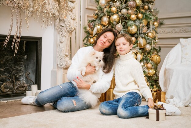 Glückliche Familienmutter und Sohn sitzen in der Nähe eines Weihnachtsbaumes mit einer Hundefrau mit Familie bei ...