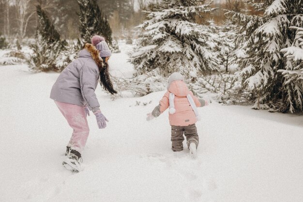 Glückliche Familienmutter und Tochter haben Spaß beim Spielen im Winter im Freien. Familie im Winterwald