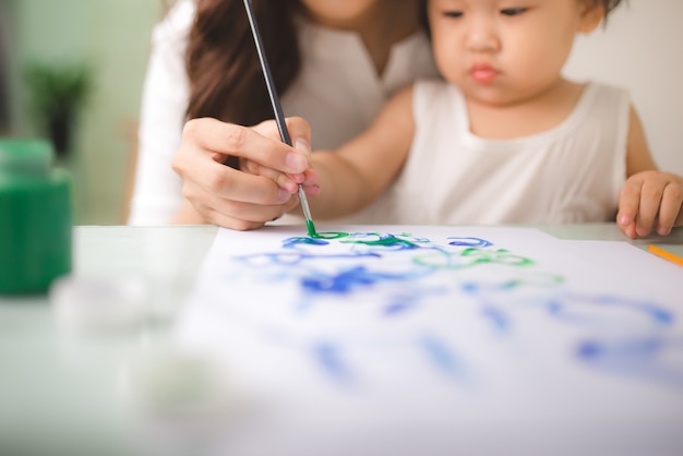 Glückliche Familienmutter und Tochter malen zusammen. Asiatische Frau hilft ihrem Kindermädchen.