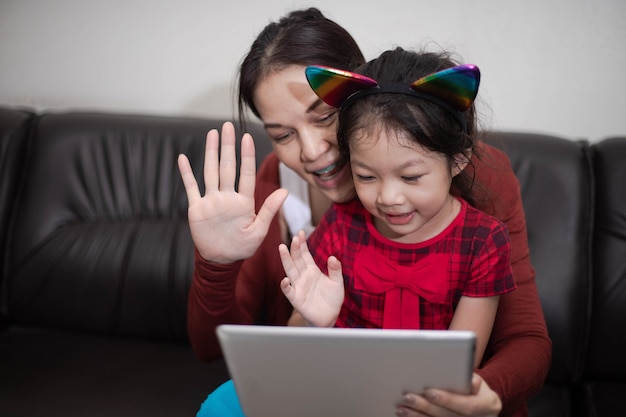 Glückliche Familienmutter und Tochter mit digitalem Tablet, das auf dem Sofa sitzt, studiert zu Hause online.