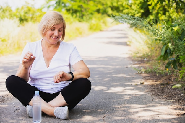 Foto glückliche fitnessfrau, die mit gekreuzten beinen und einer flasche wasser in der nähe ihres l...